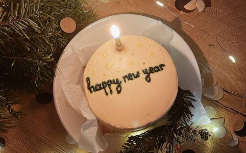 cake with the inscription happy new year with a burning candle on the background of lights and confetti